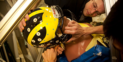 Students putting football helmet on crash dummy