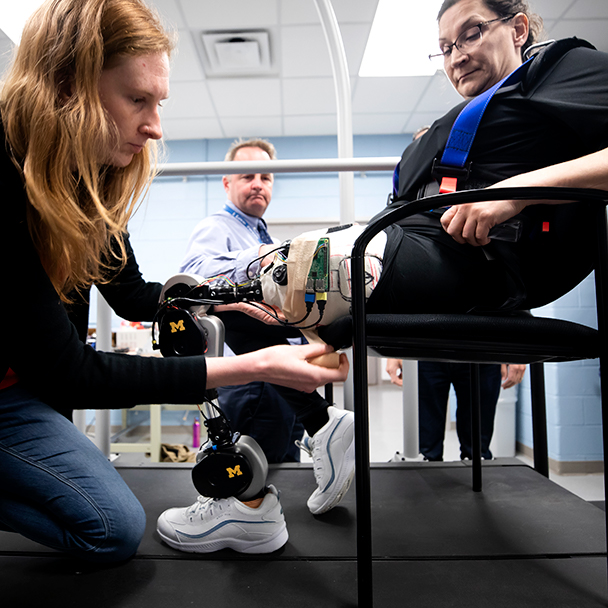 Mechanical engineering students helping a woman with a robotic leg
