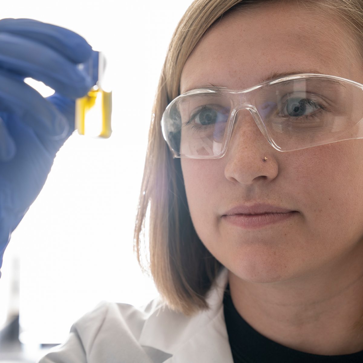 Female scientist looks at vial of a yellow liquid